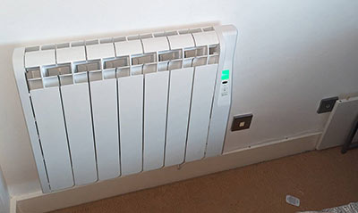 A white electric radiator installed on a wall, featuring a green indicator light.