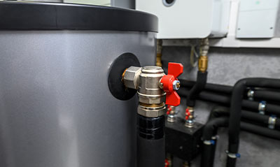 Close-up of a valve connected to a water storage tank, with red handle and surrounding pipes. Ideal for plumbing and heating discussions.