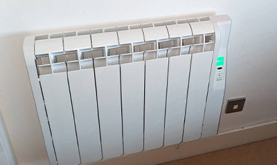 white electric radiator mounted on a wall with a control panel and a green light indicator