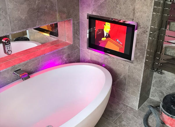 Modern bathroom featuring a freestanding tub, a wall-mounted TV displaying animated content, and stylish lighting. Ideal for luxury relaxation.