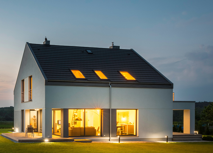 Modern two-story house with lit windows, showcasing sleek design and a grassy yard at dusk. Ideal for contemporary living.