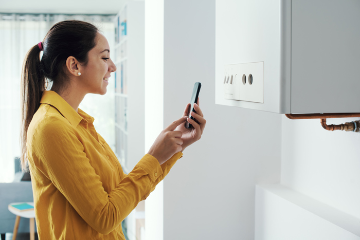 Woman in yellow shirt using smartphone to inspect home heating system. Energy efficiency check.