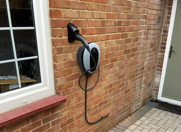 Electric vehicle charging station mounted on a brick wall, with a coiled cable and connector hanging down.