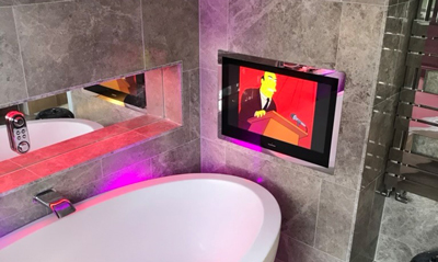 modern bathroom featuring a sleek bathtub and a flat-screen TV mounted on the wall, displaying an animated character in a colorful scene