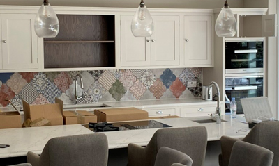 modern kitchen with white cabinets, decorative patterned backsplash, marble countertop, and glass pendant lights