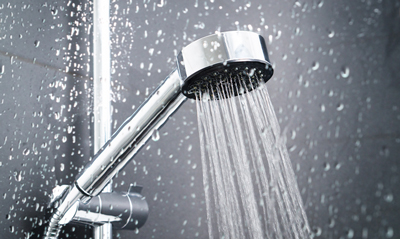 Showerhead spraying water with drops on a dark background, showcasing a modern bathroom design.