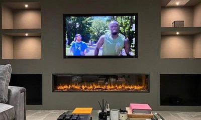 Living room with a modern design featuring a large flat-screen TV mounted on the wall, showing men jogging in a park, and a sleek, linear electric fireplace underneath, surrounded by stylish decor items.