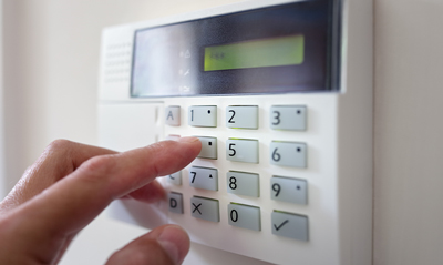 A close-up image of a hand pressing a button on a security keypad, with a display screen showing numbers and options.