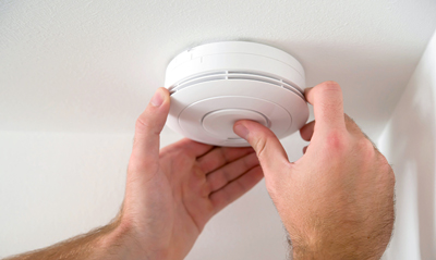 Person installing a smoke detector on the ceiling, focusing on home safety and maintenance.