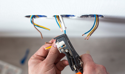 Person using wire strippers on electrical wires in a wall, demonstrating home electrical repair techniques.