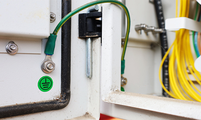 Close-up of electrical connections with green grounding wire and terminals in a control panel, showcasing electrical equipment and safety features.