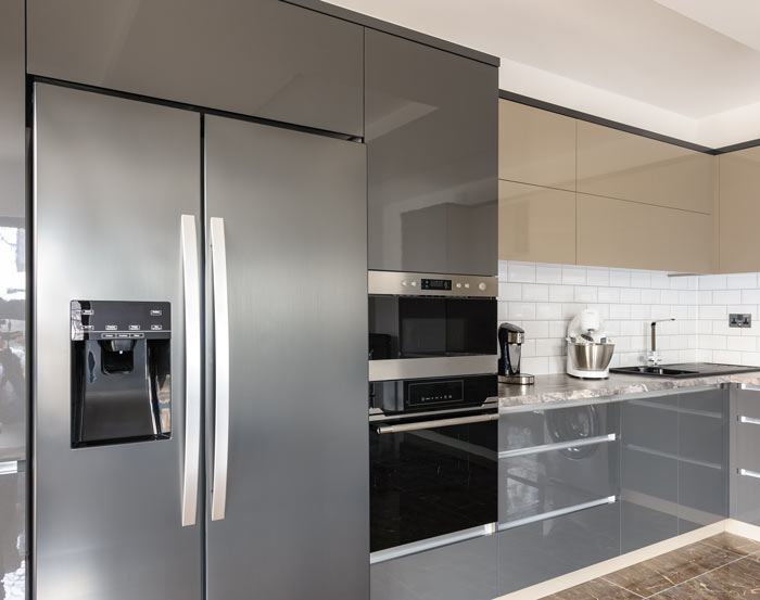 modern kitchen with sleek gray cabinets and stainless steel appliances, featuring a refrigerator with ice dispenser, a built-in oven, and a stylish countertop